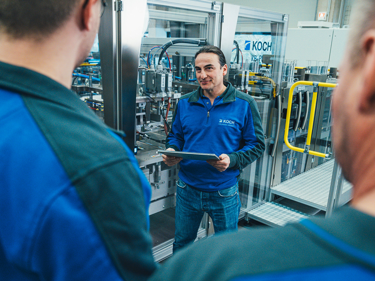 KOCH employee with a tablet talking to colleagues in front of a packaging machine